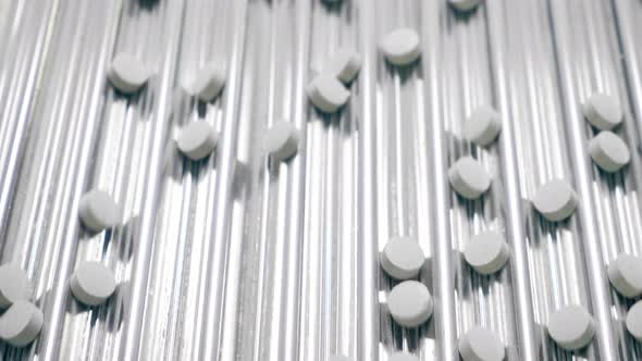 White Tablets are Getting Transported By a Conveyor Mechanism alt
