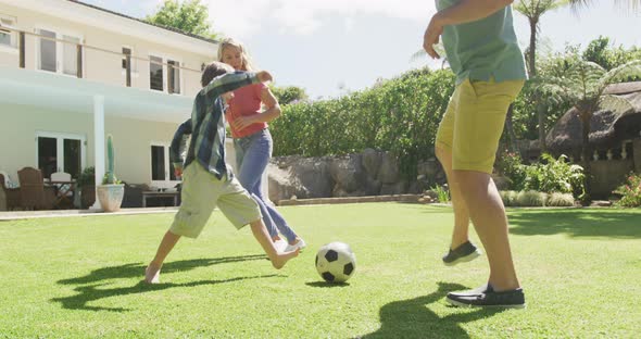 Happy caucasian couple with son playing football in garden alt