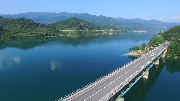 Red car driving on bridge over lake alt