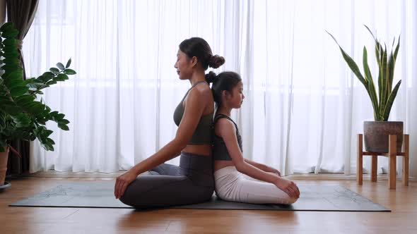 Healthy woman trainer training a little girl to yoga pose and exercise at home.
