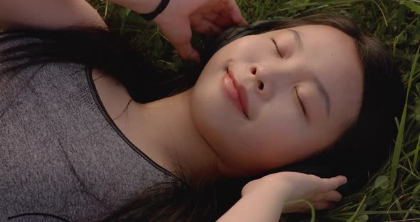 Beautiful Young Asian Female Wearing Sunglasses and Headphones While Lying on the Floor Grass