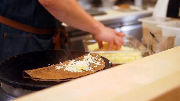 Chef sprinkling cheese on crepe alt