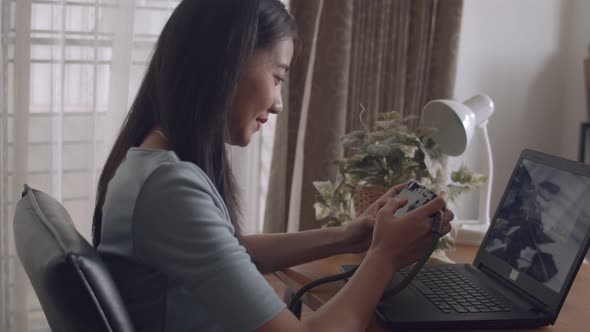 Beautiful young Asian woman sitting on table checking her photo after taking a photo at home.