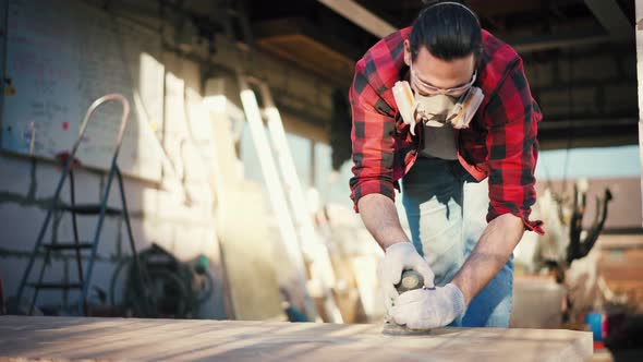 A Young Man in a Construction Respirator Grinds a Parquet Board with a Sander alt
