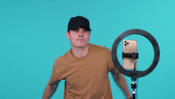 Young Guy Video Blogger Dances to the Music on a Blue Background and Takes a Selfie Video on alt