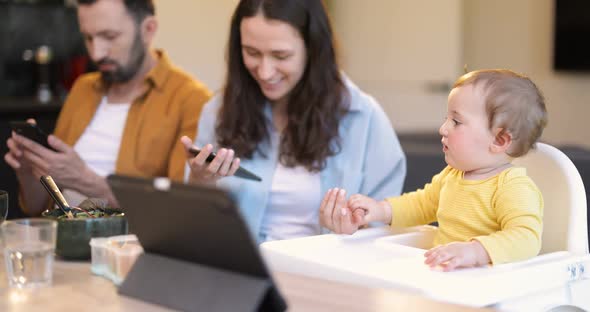 Baby and Parents Busy in a Digital Gadgets During a Lunch at Home alt