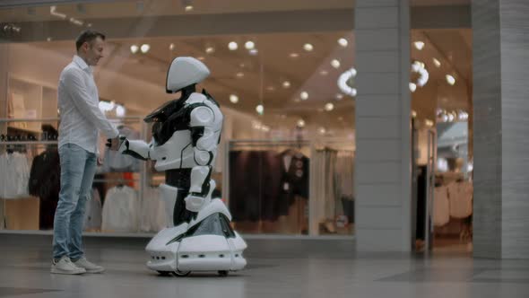 A Man Stands with a Robot Bot and Asks Him Questions and Asks for Help By Clicking on the Screen on alt