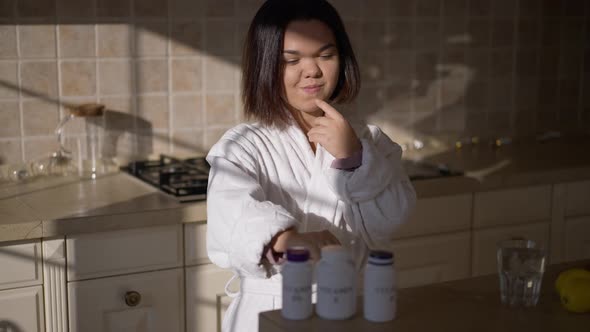 Brunette Positive Little Woman Choosing Vitamins Standing on Sunny Kitchen at Home alt