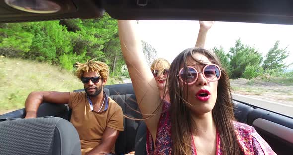 Cheerful multi ethnic students enjoying vacation driving in red convertible alt