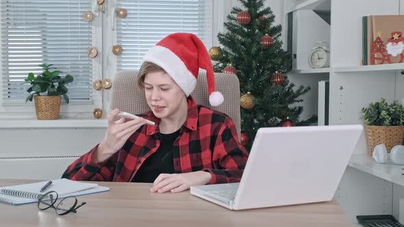 A Cheerful Teenage Boy in a Santa Claus Hat Chatting on a Mobile Phone During the Christmas Holidays