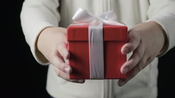 Little Girl's Hands Giving Red Gift Box with White Ribbon