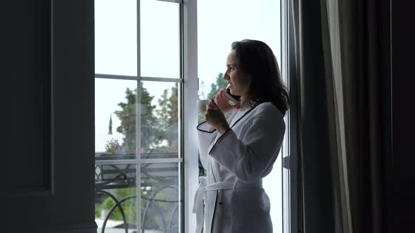 Woman in Bathrobe Talking By Phone at Hotel Room alt