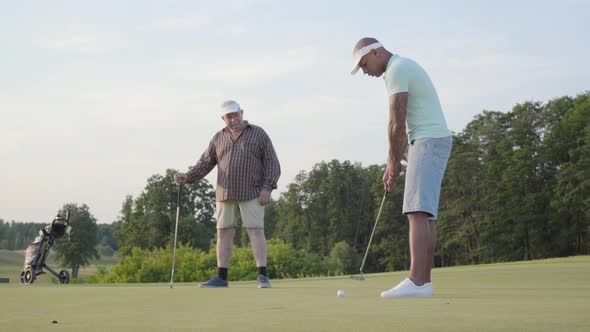 Mature Caucasian Man and Young Middle Eastern Man Playing Golf on the Golf Field alt