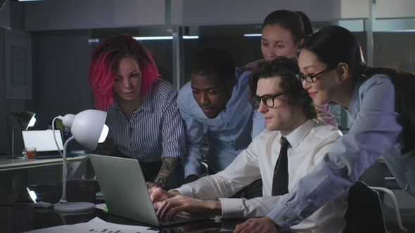Multiethnic Colleagues Work on Startup Project Together Using Laptop Late at Night alt