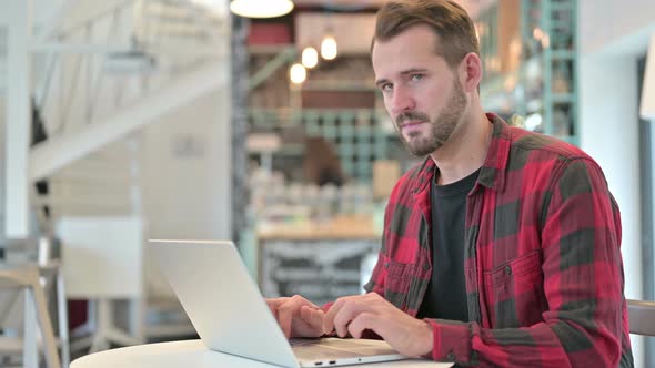 Thumbs Down By Disappointed Young Man with Laptop in Cafe  alt