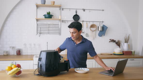 Man Using Air Fryer and Laptop in Kitchen alt