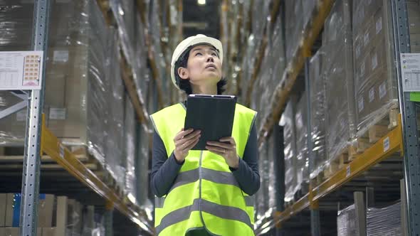 Young Asian Woman Is Using Tablet Standing in Warehouse During Working Day alt
