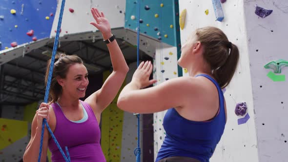 Two caucasian women talking and high fiving at indoor climbing wall alt
