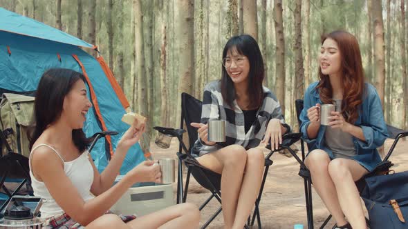 Group of young asia camper friends sitting in chairs by tent in forest.