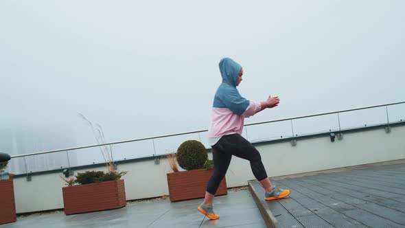 Sport Woman in Sportswear Wears Hood Doing Workout Step Cardio Exercising Training on Roof of House alt