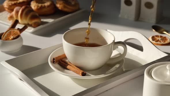 Tea is Poured Into a White Mug or Cup on a White Light Background with Fresh Pastries and Croissants