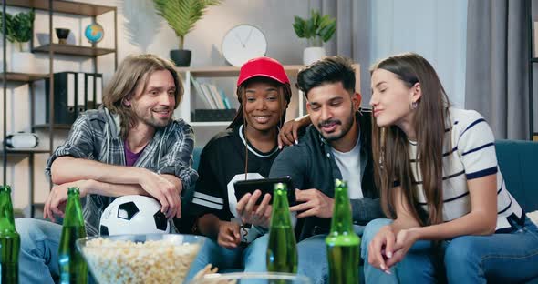 Young Mixed Race People Sitting on the Couch at Home and Use Smartphone to Watch Funny Videos alt