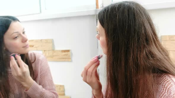 Young Beautiful Woman Puts Powder on Her Face with a Brush in Front of the Mirror.