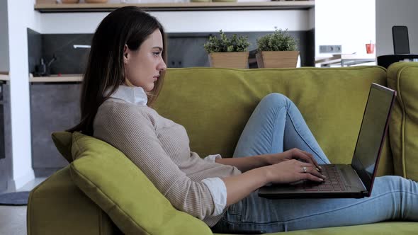 Young Woman in a Beige Sweater Relaxing on the Couch While Holding a Laptop at Home Office alt