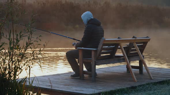 Man Holding Fishing Rod Sitting on the Riverside