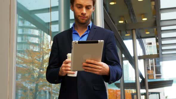 Businessman holding coffee cup and using digital tablet alt