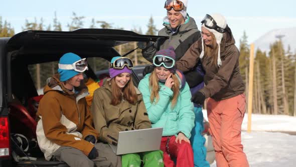 Group of young snowboarders on the slopes using laptop alt