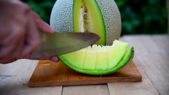The man use knife split the green melon on wood plate alt