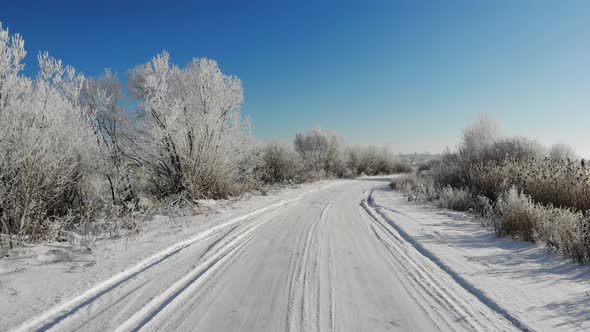 Snowy country road between trees and bushes. Winter time. Zoom in, hand held alt