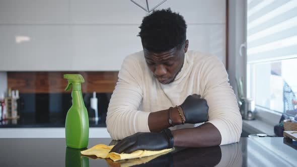 Tired Young Black Man Resting on the Kitchen Cupboard While Cleaning alt