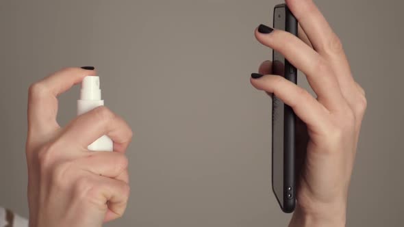 Slow Motion. Woman Sprays Disinfecting Solution on Mobile Phone at Home.