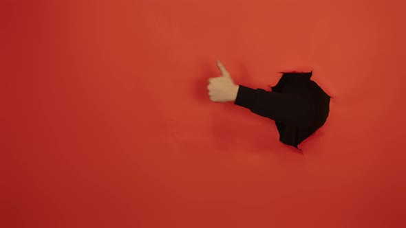 Man's Hand Showing Thumb Up and Sticking Out of Hole of Orange Background alt