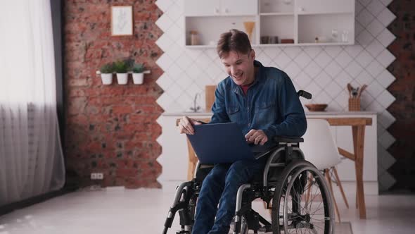 Adult Man in Wheelchair Using Modern Laptop at Home