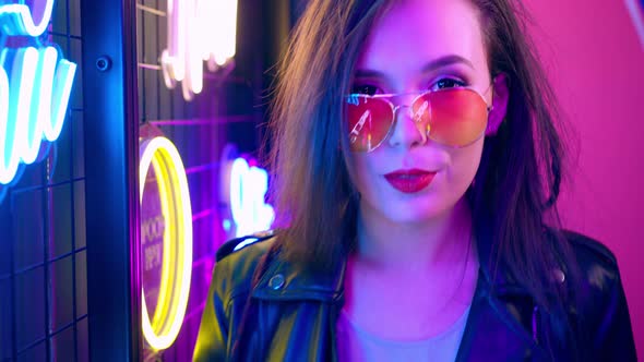 Mixed Raced Woman with Dreadlocks and Glasses Posing Near Glowing Neon Wall in the Dark alt