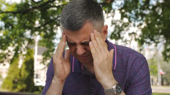 A Man Outside is Massaging His Temples As a Result of a Severe Headache