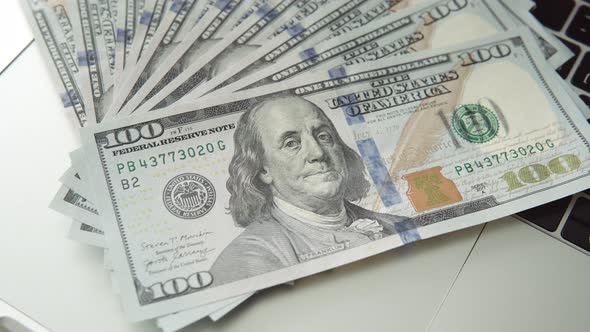 A Fan of Banknotes 100 Dollar Bills Lie on an Expensive Modern Laptop Closeup