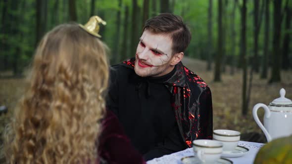 Caucasian Man with Halloween Makeup Looking at Girl with Long Hair Sitting in Forest alt