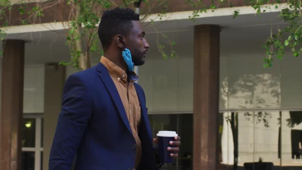 African american businessman with face mask walking in city street alt