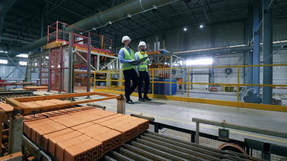 Male Engineers Walk at a Modern Industrial Plant, Checking Pallets with Bricks. alt