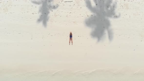 Aerial: Woman relaxing on white sand beach turquoise water tropical coastline alt