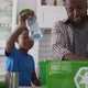 Happy african american father and son standing in kitchen putting plastic rubbish in recycling box - VideoHive Item for Sale