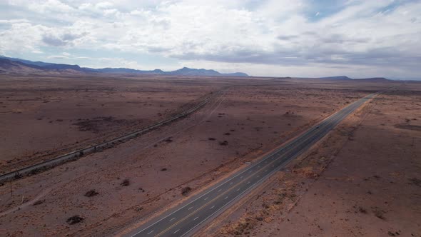 Drone shot of a railroad and highway in the desert with one car on the road alt