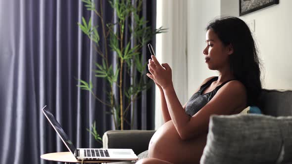 Pregnant Woman Sitting on the Sofa Taking Selfie and Photos of Her Big Tummy alt