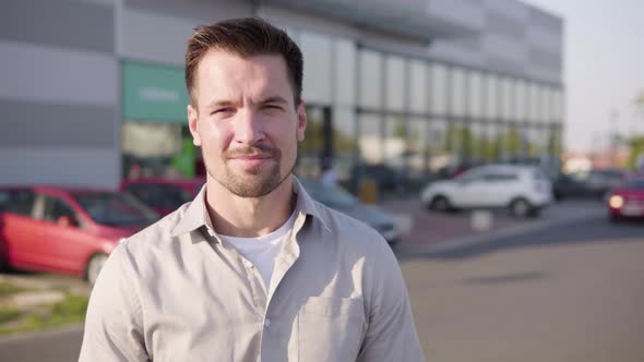 A Young Caucasian Man Shows a Thumb Up to the Camera and Nods with a Smile in an Urban Area alt