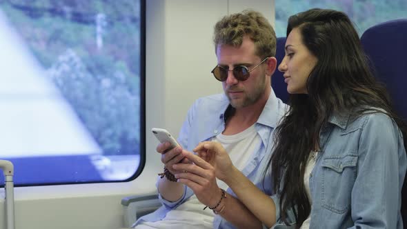 Couple Is Viewing Pictures in Smartphone Riding By Suburban Train alt