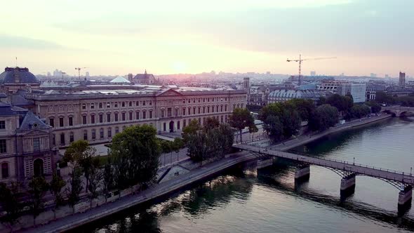 Morning aerial footage of Louvre museum and Pont des Arts bridge over Seine river. Drone flying down alt